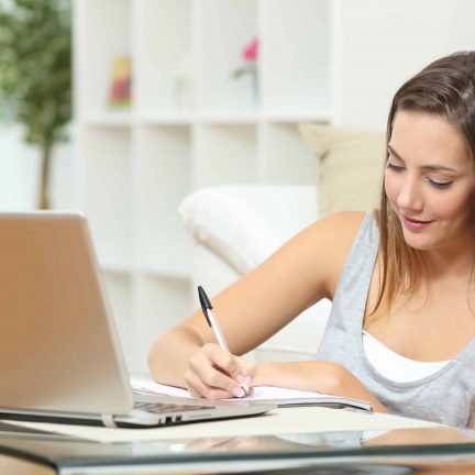 Vrouw schrijft op een notitieblok bij een laptop
