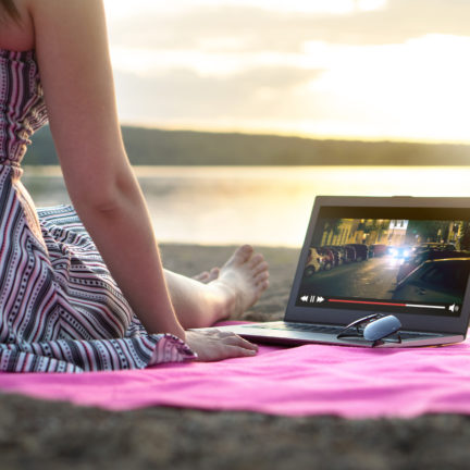 Vrouw kijkt televisie op haar laptop op een strand