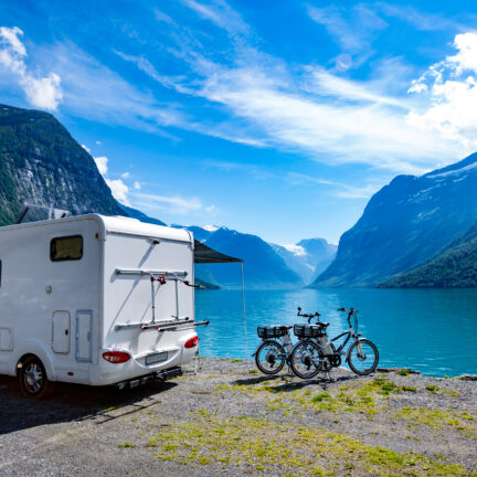 Witte camper met fietsen aan een meer en bergen in de verte