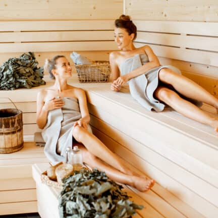 Twee vriendinnen in badhanddoek zitten te ontspannen in de sauna