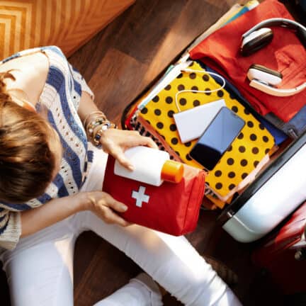 Vrouw pakt EHBO-kit en SPF in in open reiskoffer